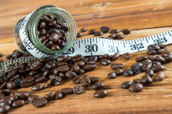 Coffee bean in glass bottle with tape measure on wooden backgrou — Stock Photo, Image