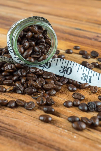 Coffee bean in glass bottle with tape measure on wooden backgrou — Stock Photo, Image