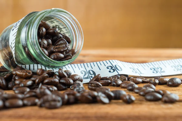 Coffee bean in glass bottle with tape measure on wooden backgrou — Stock Photo, Image