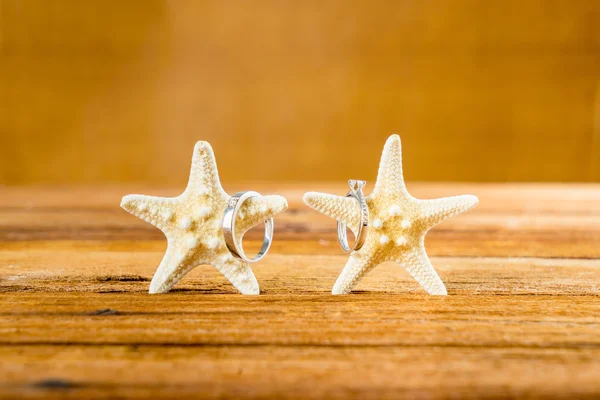 Dua cincin pernikahan dengan dua bintang laut di atas meja kayu Stok Gambar Bebas Royalti