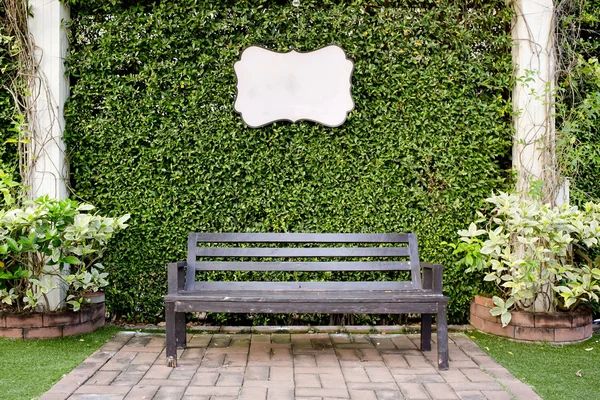 Wooden dark brown bench and blank vintage card against green lea — Stock Photo, Image