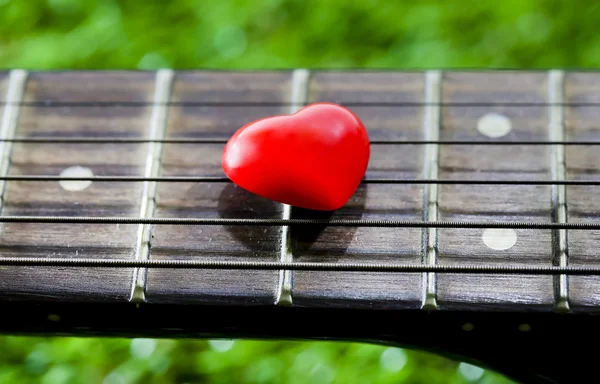 Srdce na krk kytary a smyčce na trávě — Stock fotografie
