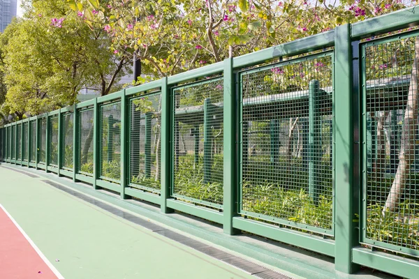 Running track and a green steel fence with garden. — Stock Photo, Image