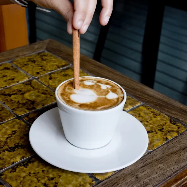 A coffee cup Latte being stirred by Cinnamon sticks.