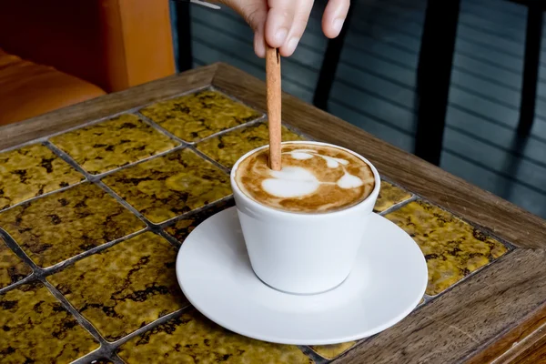 A coffee cup Latte being stirred by Cinnamon sticks. — Stock Photo, Image