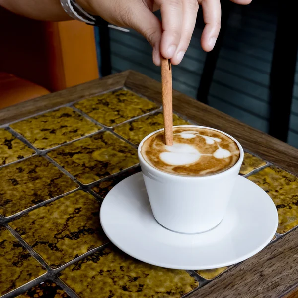 A coffee cup Latte being stirred by Cinnamon sticks. — Stock Photo, Image