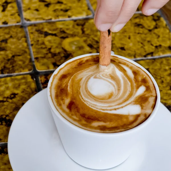 A coffee cup Latte being stirred by Cinnamon sticks. — Stock Photo, Image