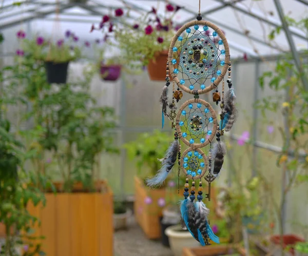 Beautiful handmade boho styled dreamcatcher with feathers and beads against flowers and plants. Mystic background with dream catcher, esoteric and occult concept