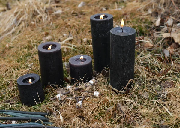 Magic ritual with burning black candles in the grass.  Esoteric, gothic and occult background, Halloween mystic and wicca concept outdoors.