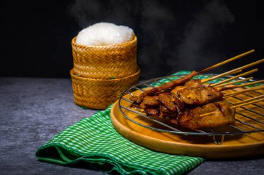 Çelik ızgaraya konmuş bambu şiş üzerinde ızgara domuz eti, ahşap bir tepside, arabada pilav, servis etmeye hazır.