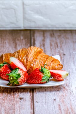 Avrupai kahvaltı ahşap bir masada beyaz bir tabakta kruvasan ve taze çileklerden oluşur..