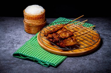 Çelik ızgaraya konmuş bambu şiş üzerinde ızgara domuz eti, ahşap bir tepside, arabada pilav, servis etmeye hazır.