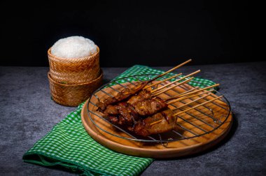 Çelik ızgaraya konmuş bambu şiş üzerinde ızgara domuz eti, ahşap bir tepside, arabada pilav, servis etmeye hazır.