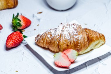 Kremalı şeker ve taze çilek serpiştirilmiş kruvasanlardan oluşan kıtasal bir kahvaltı..