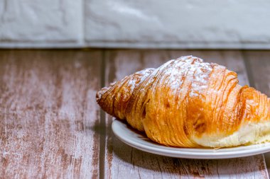 Tahta bir masada beyaz bir tabakta krema serpiştirilmiş kruvasanlar..