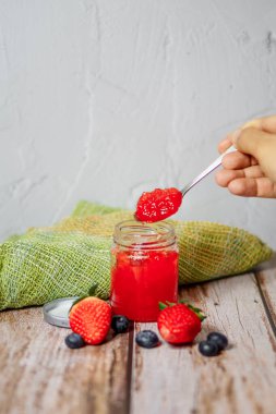 Çilek reçeli ve çilek meyvesi ahşap bir masaya konur.