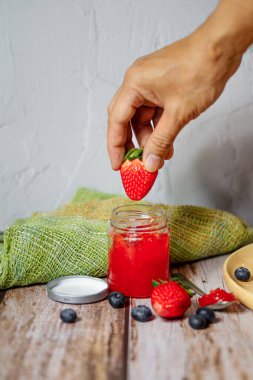 Çilek reçeli ve çilek meyvesi ahşap bir masaya konur.