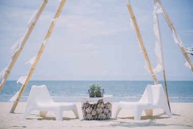 İki beyaz sandalye ve kumlu plajda deniz zeminine karşı bir masa.