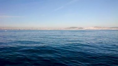 Denizden İstanbul 'a harika bir manzara. Suda büyük tepeler, şamandıralar ve küçük yatlar görebilirsiniz. Açık mavi gökyüzü ufuktaki şehirde kayboluyor. Kamera yana hareket ediyor..