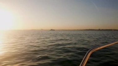 Gün batımında nefis deniz manzarası. Günbatımı suyu altın rengine boyar, parlak bir yol su yüzeyinde güneşe doğru uzanır. Gökyüzü, bir tarafta mavi, diğer tarafta ve ufukta turuncuya dönüyor. Kamera soldan sola hareket ediyor..