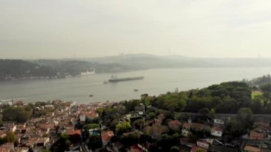 İstanbul 'un Arnavutkoy bölgesinde yakalanan Boğaz' ın nefes kesici insansız hava aracı görüntüsü. Tepelerde bir sürü ev ve ağaç var. Ufukta, yüksek tepeler sisle kaplı. Büyük bir kargo gemisi boğazdan geçiyor.. 