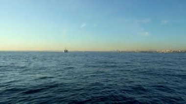 Mavi denizin insansız hava aracı görüntüsü. Şehir ufukta görünür, ufuktaki gökyüzü soluk sarı, güzel bir gündoğumu. İnsansız hava aracı ilerliyor.