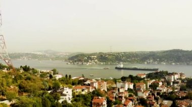 İstanbul 'un Arnavutkoy bölgesinde yakalanan Boğaz' ın insansız hava aracı görüntüsü inanılmaz. Yamaçlarda bir sürü ev ve ağaç var. Ufukta yüksek bir tepe var. Büyük bir kargo gemisi boğazdan geçiyor. İHA yavaşça yükseliyor.