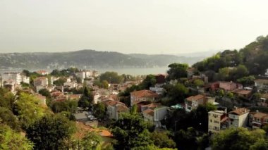 Stanbul 'un Arnavutkoy ilçesindeki evlerin insansız hava aracı görüntüsü. Alçak katlı evler ağaçların arasındaki yamaçlarda duruyor. İnsansız hava aracı tepeden tırnağa hareket ediyor, doğrudan ağaçlara düşüyor.