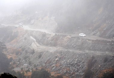 A vehicle negotiating the rough road covered with fog and mist during monsoon at Kyongsla situated at 11,500 ft altitude in East Sikkim, India.