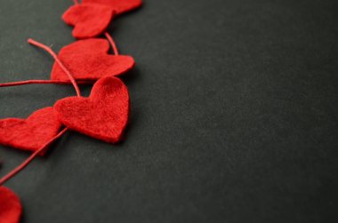 Örtüden oyulmuş beş kırmızı kalp ve siyah arka planda kırmızı bir balmumu kablosu.