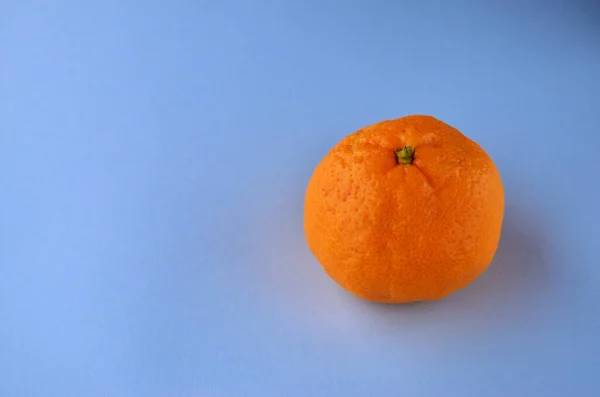 One orange tangerine in the peel on a blue background with a copy space — Stock Photo, Image