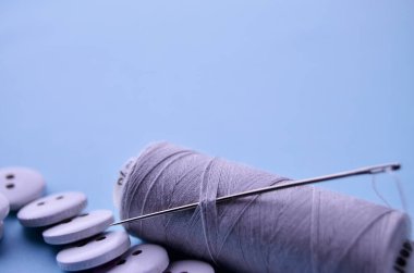 Üzerinde iğne olan gri bir iplik, afişin alt kenarına saplanmış ve saçılmış beyaz düğmeler, mavi arka planda bir kopya alanı ile birlikte.