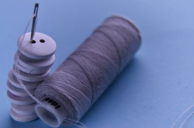 Düğmeler beyaz ahşap, iğne ve gri iplikçikli mavi arka planda.