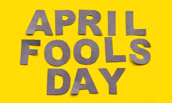 Legenda da imagem April Fools Day feito de letras de papel cinza em um fundo amarelo close-up — Fotografia de Stock