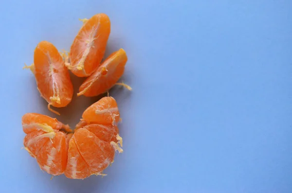 Uma tangerina descascada fresca com três cunhas separadas na mesa é uma vista de cor azul de cima com um espaço de cópia — Fotografia de Stock