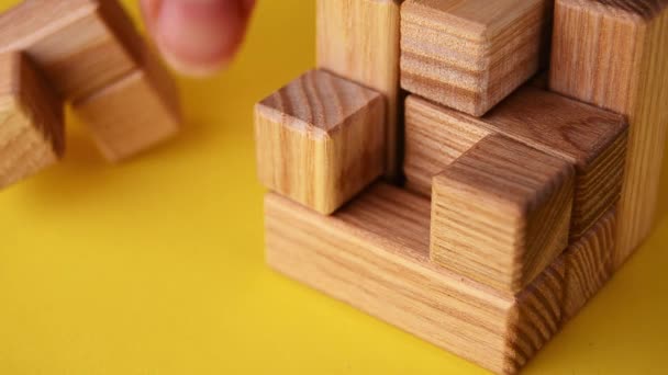 Video puzzle logico di legno da vicino su uno sfondo giallo, la mano mette l'ultimo elemento — Video Stock