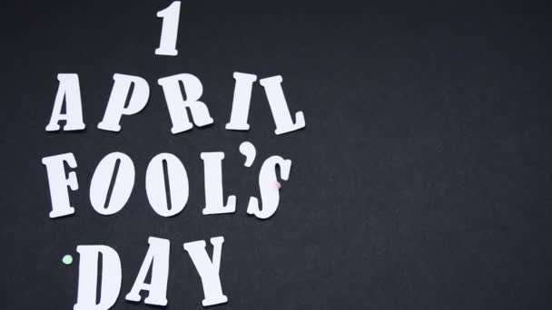 Подпись под видео April 1 white on a black background sprinkled with multi-colored confetti — стоковое видео