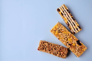 Üç çubuk granola fanı sağ alt kenarda duruyor. Mavi arkaplanda bir kopya alanı var.