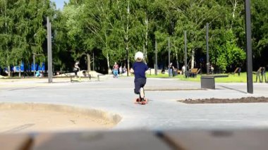 Videoda motosikletli bir çocuğun parktaki bir patika boyunca uzaklaşıp uzaklaşırken görüntüsü var. Rusya Embankments Chelny, 15.09.2020