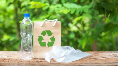 Plastik su şişeleri, plastik torbalar ve geri dönüşümlü logoları yeşil bokeh 'in arkasındaki ahşap bir masaya yerleştiriliyor. Kavram geri dönüşümü temiz gezegeni ve ekoloji kavramını kurtardı.
