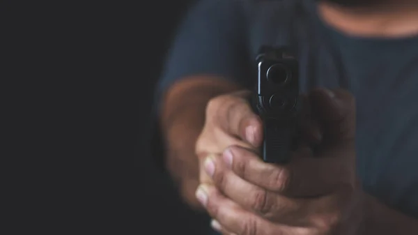 Man holding a gun in his hand with a black background, rearview. Man with a pistol in his hand aims his target.