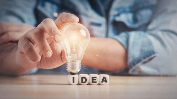 Man hand holding a light bulb on a wooden block with Word Ideas. innovation concept.
