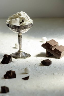 Gümüş kaplama dondurma ve siyah çikolata parçalarıyla sanatsal bir hayat. Güneş ışığı beyaz desenli zeminde derin gölgeler oluşturuyor..