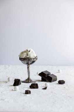 Lezzetli stracciatella dondurması, içinde çikolata parçacıkları olan gümüş bir kadeh. Beyaz desenli masa üzerinde güneşli yaz tatlı kompozisyonu.