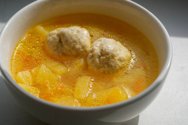 Güneş ışığı altında beyaz bir kasede patates ve havuçlu ev yapımı köfte çorbası. Lezzetli yemek..