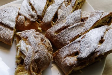 Sliced pieces of apple strudel with powdered sugar on a white plate. Homemade sweet pastry serving.