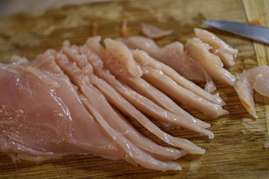 Tahta kesme tahtasında dilimlenmiş çiğ tavuk göğsü filetosu. Pişirmek için taze tavuk eti şeritleri..