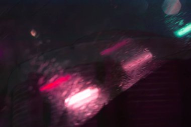 Yağmurlu bir pencereden gece şehir ışıklarının soyut bir görüntüsü,