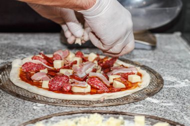 Pastırma ya da jambon dilimlenmiş pizzayı peynirli ve soslu çiğ pizzaya koyuyor. Etsever pizzayı hazırlıyorum..