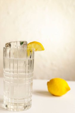 Su ve limon dilimli kristal viski bardağı beyaz desenli duvara karşı. Şık içki fotoğrafçılığı..